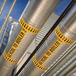 Industrial pipes are marked with bright yellow labels that say 'glycol to boiler.'