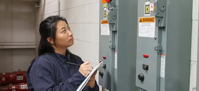 An employee taking notes on an electrical panel's compliance with OSHA electrical panel clearance requirements.