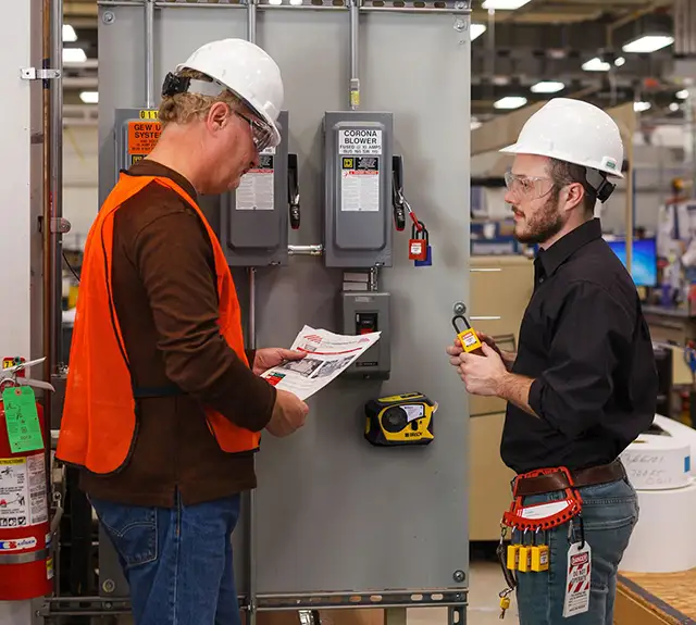 Two warehouse workers going over proper OSHA electrical panel clearance requirements as part of compliance upkeep.